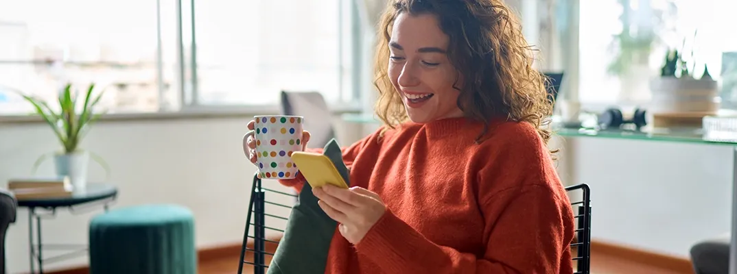 Girl looking at a cell phone with a mug in her hand