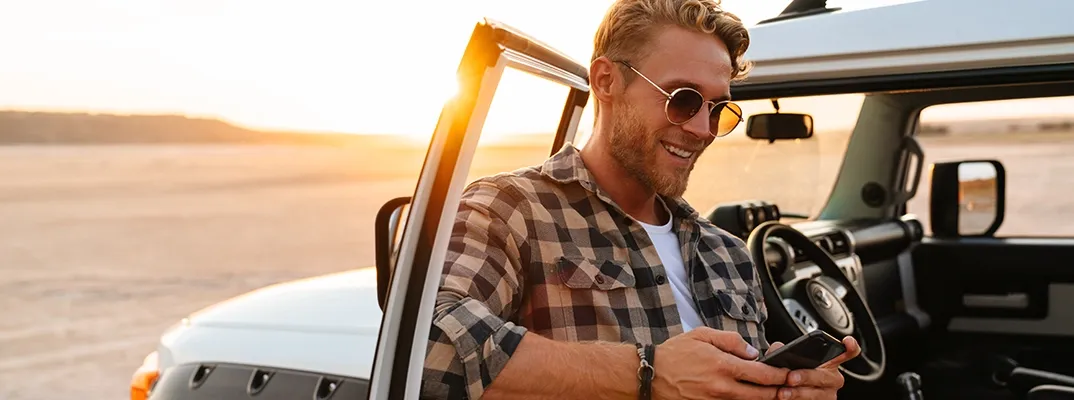 A man leaning on a truck door looking at a cellphone.