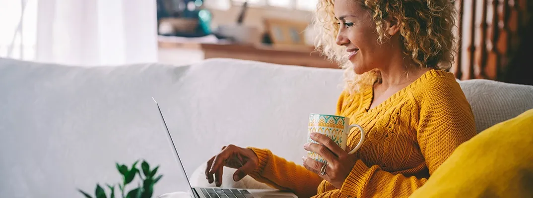 A woman sitting down with a mug and a laptop, looking at mortgage information