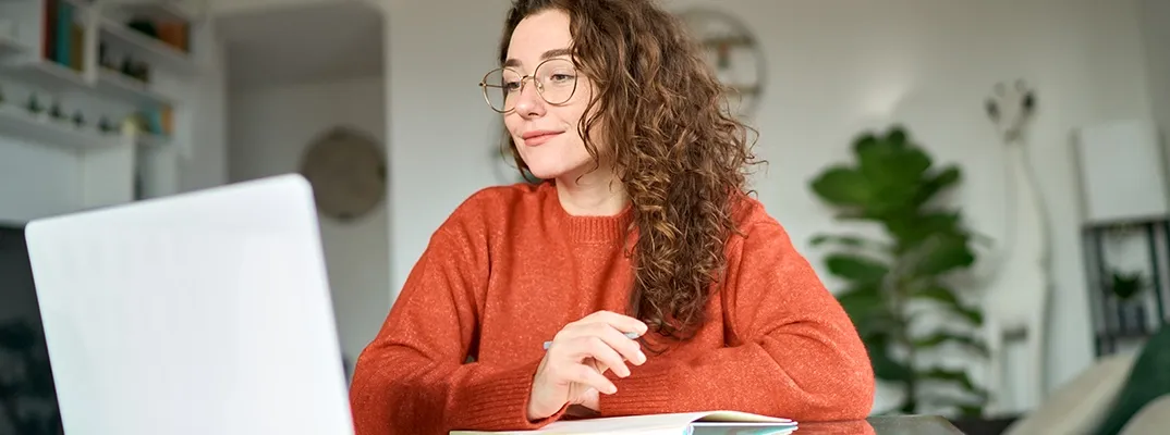 A woman with a notebook looking at a laptop