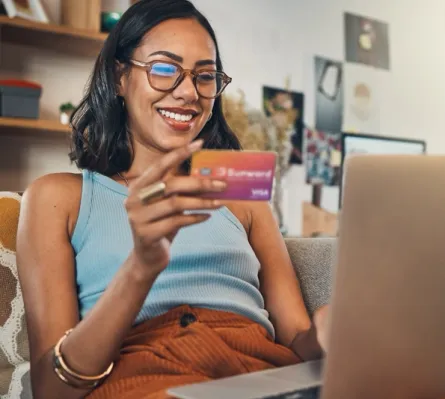 A woman with a laptop holding a Sunward Visa Signature Credit Card