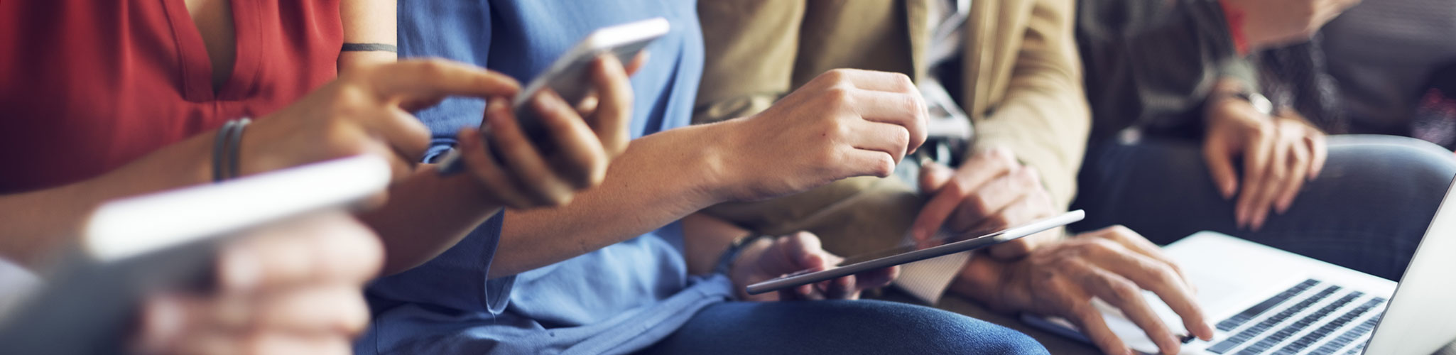 Image of several people sitting down and using cell phones, tablets, and laptops.