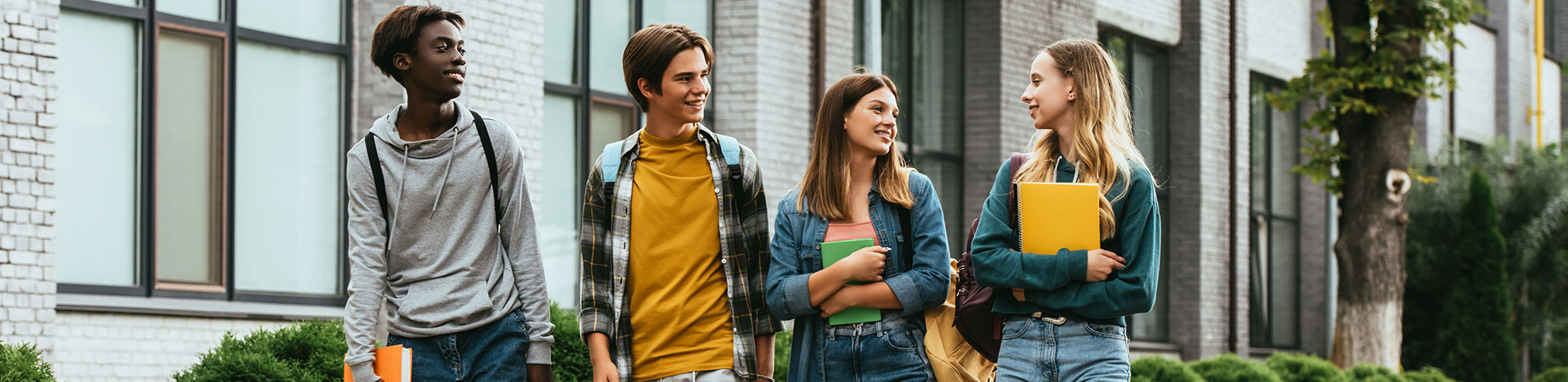 four teenagers walking together in front of a school