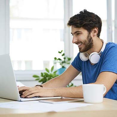 Smiling young man wearing headphones sitting at a desk with a laptop