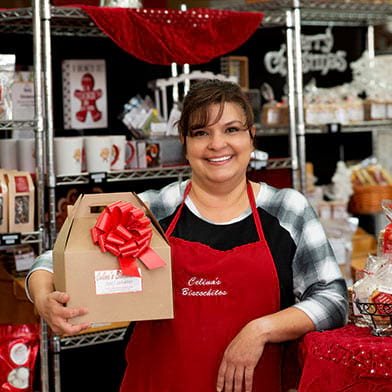 Celina Grife, owner of Celina's Biscochitos, grinning while holding gift box of biscochitos.