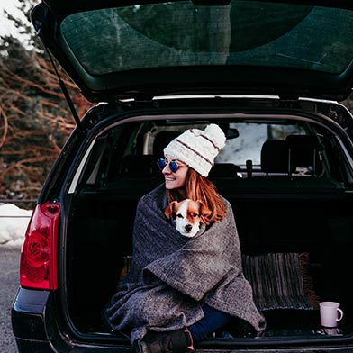 Woman with dog sitting in back of car wearing winter clothing