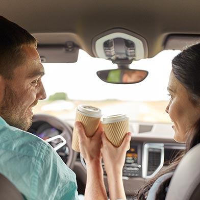 Woman, husband in car holding coffee cups and smiling at each other