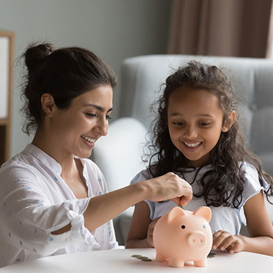 Mother and young daughter putting money into a piggy bank