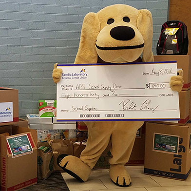 Sandy the Lab posing with donated school supply items and holding donations check.