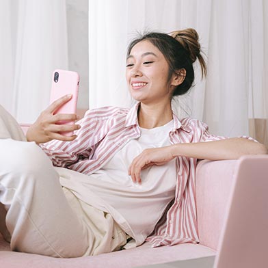 Young woman relaxing on couch and smiling while on her cellphone