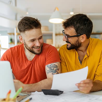 Couple sitting together at home computer happily examining paperwork