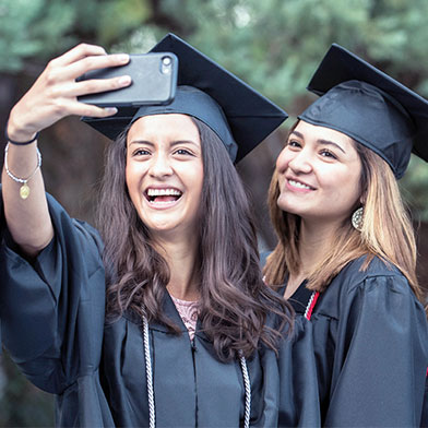 three young girls in graduation gowns taking a selfie on a cell phone.