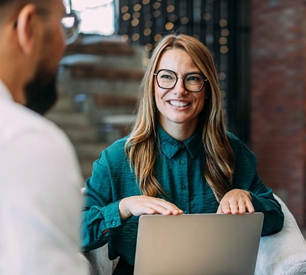 A woman with a laptop smiling at a man who is in the foreground on the left of frame