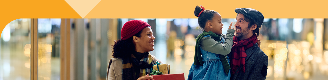 A family of three in winter clothes carrying wrapped presents