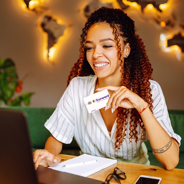 A woman with a laptop holding a Sunward Visa Platinum Rebate Credit Card